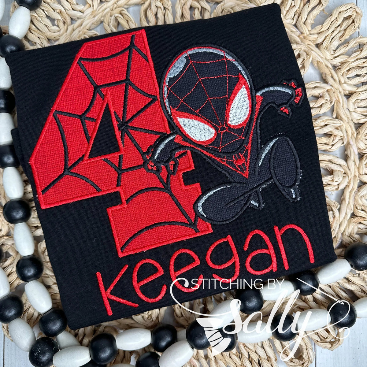 A black shirt with a custom birthday number and inspired miles spider man appliqued on it. Personalized with child’s name in red thread.