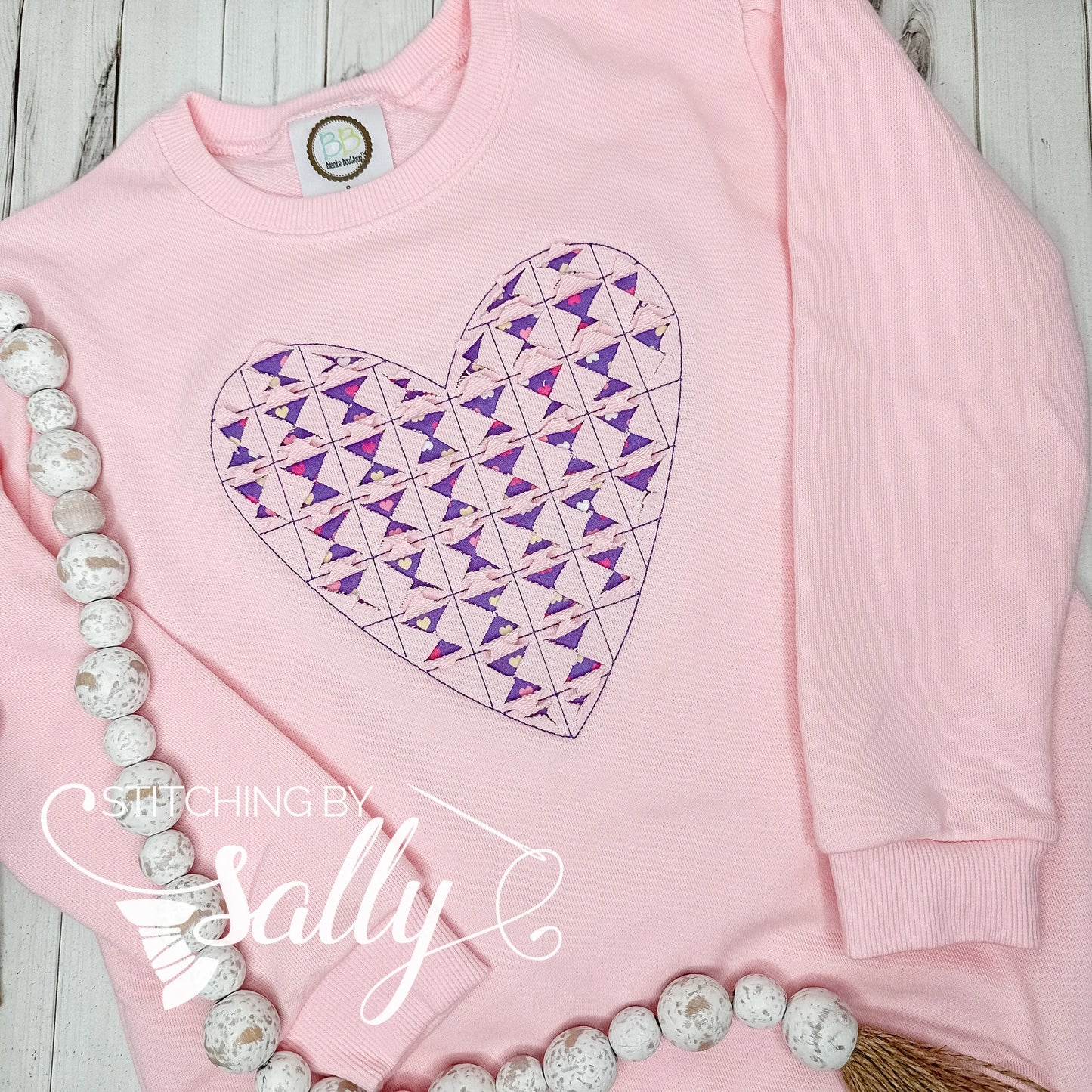 A pink sweatshirt with a reverse appliqué heart cut out revealing purple valentines fabric.