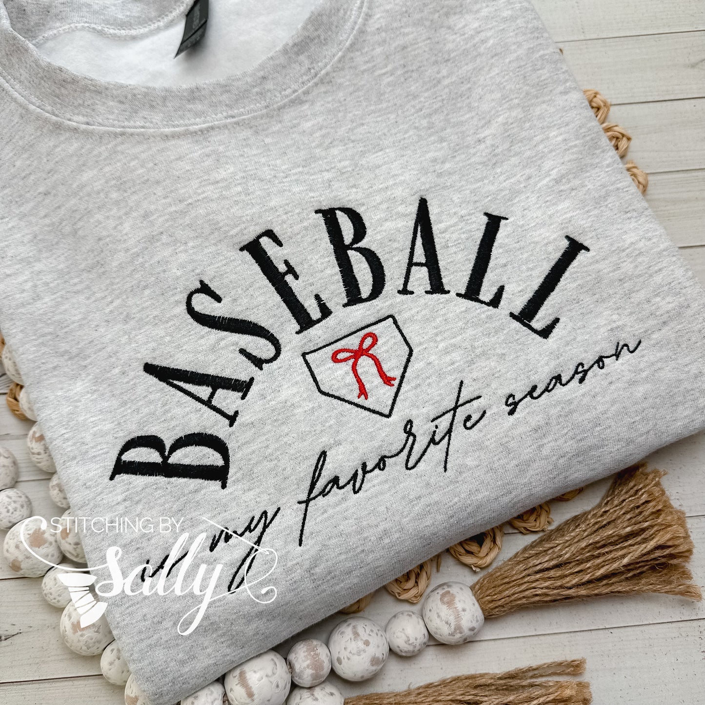 A grey sweatshirt with the words “baseball is my favorite season” embroidered on it with a cute red bow. Colors can be customized to match your favorite team!
