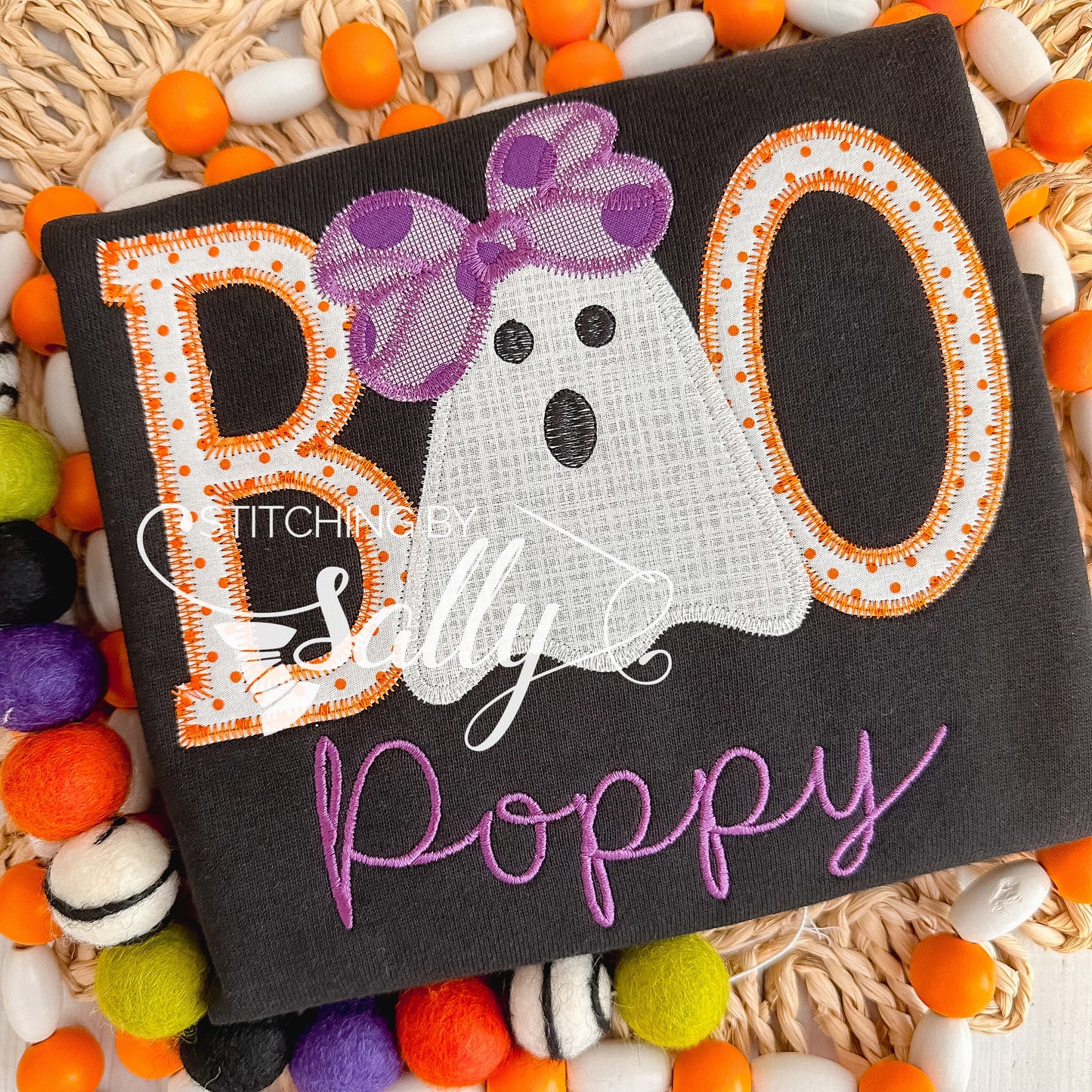 Close-up of BOO ghost appliqué detail with stitched bow accent on a black shirt.