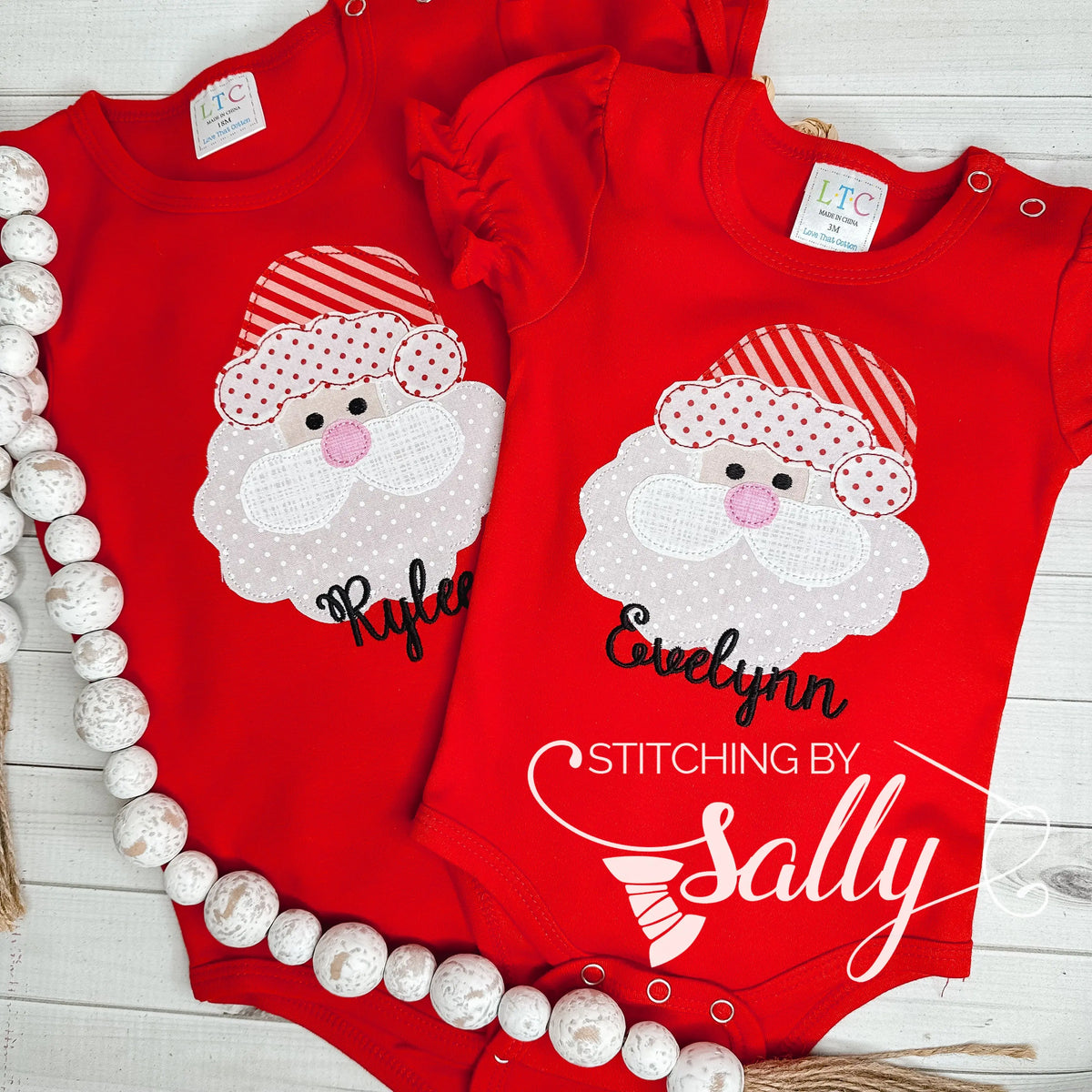 A set of matching red baby onesies with a santa face applique in red and white fabric. Both personalized with names in black thread.