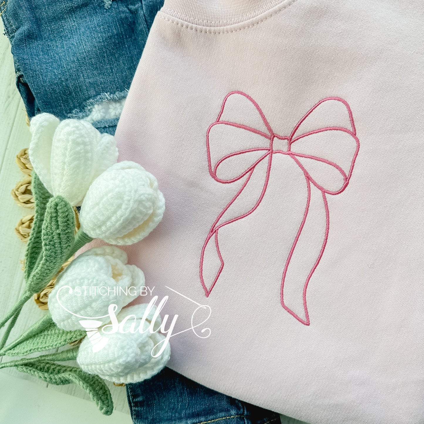 A hot pink bow embroidered on a light pink sweatshirt.