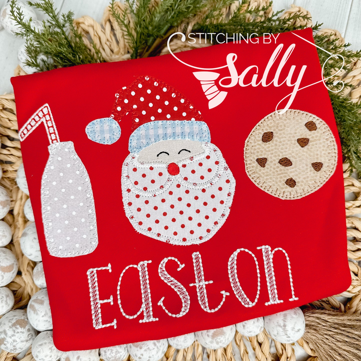 A red shirt with a milk jug, jolly santa, and a chocolate chip cookie appliquéd on. A name is embroidered underneath the design.