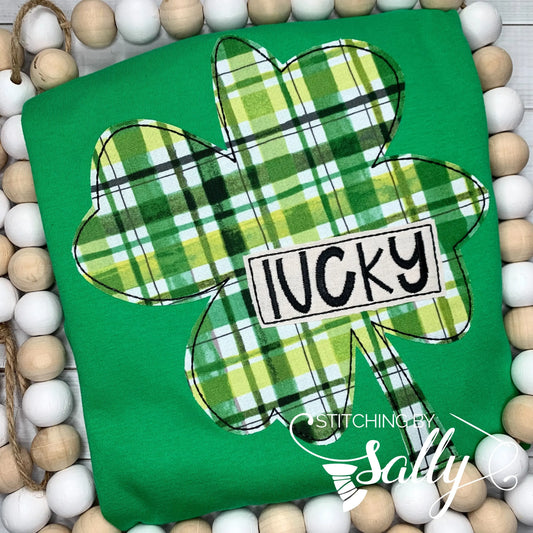 Green shirt with a 4 leaf clover appliquéd in green plaid print. Lucky is embroidered on the clover.