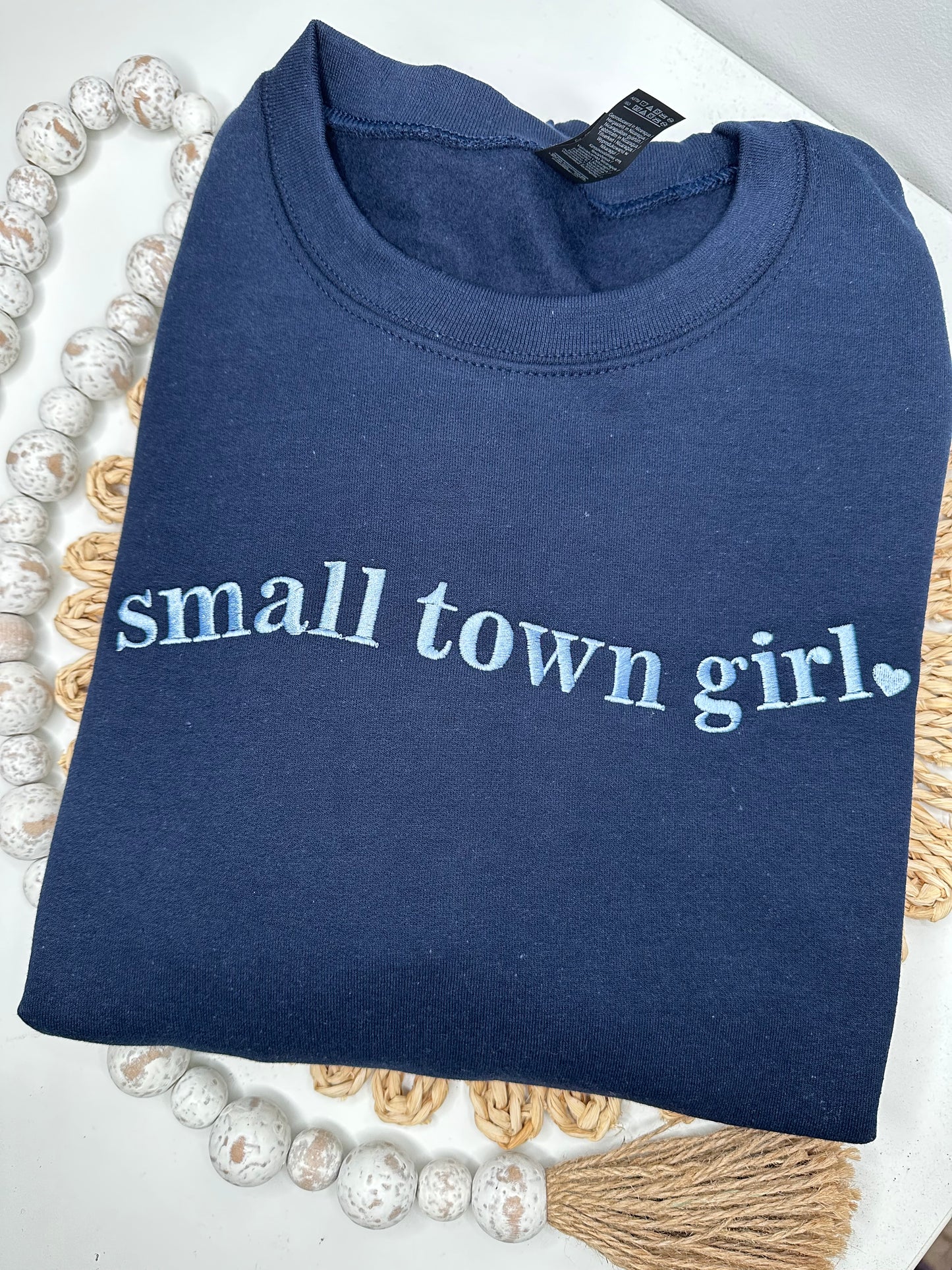 Folded navy blue sweatshirt with 'small town girl' embroidered.