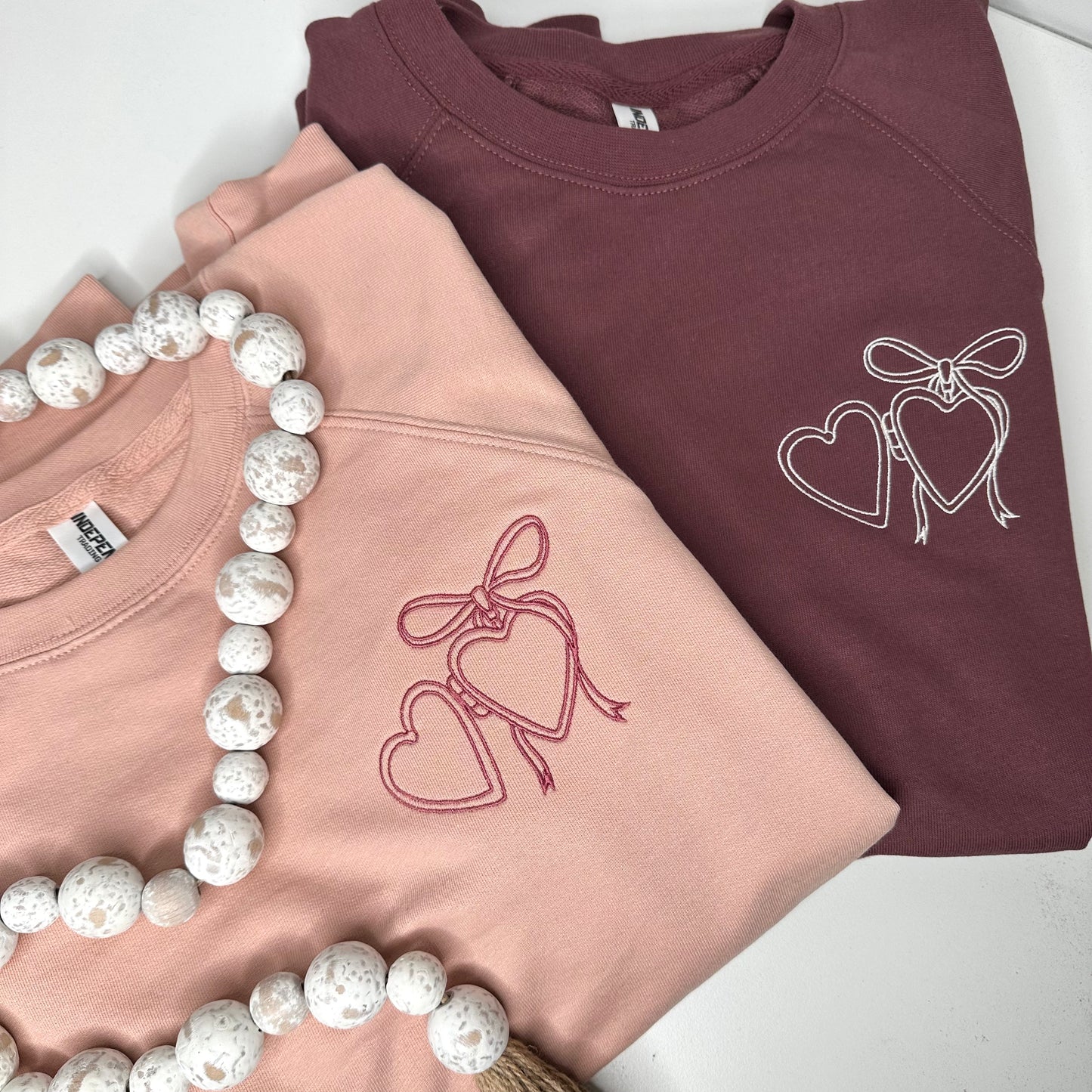 Heart locket embroidered on left chest of rose or maroon sweatshirt.