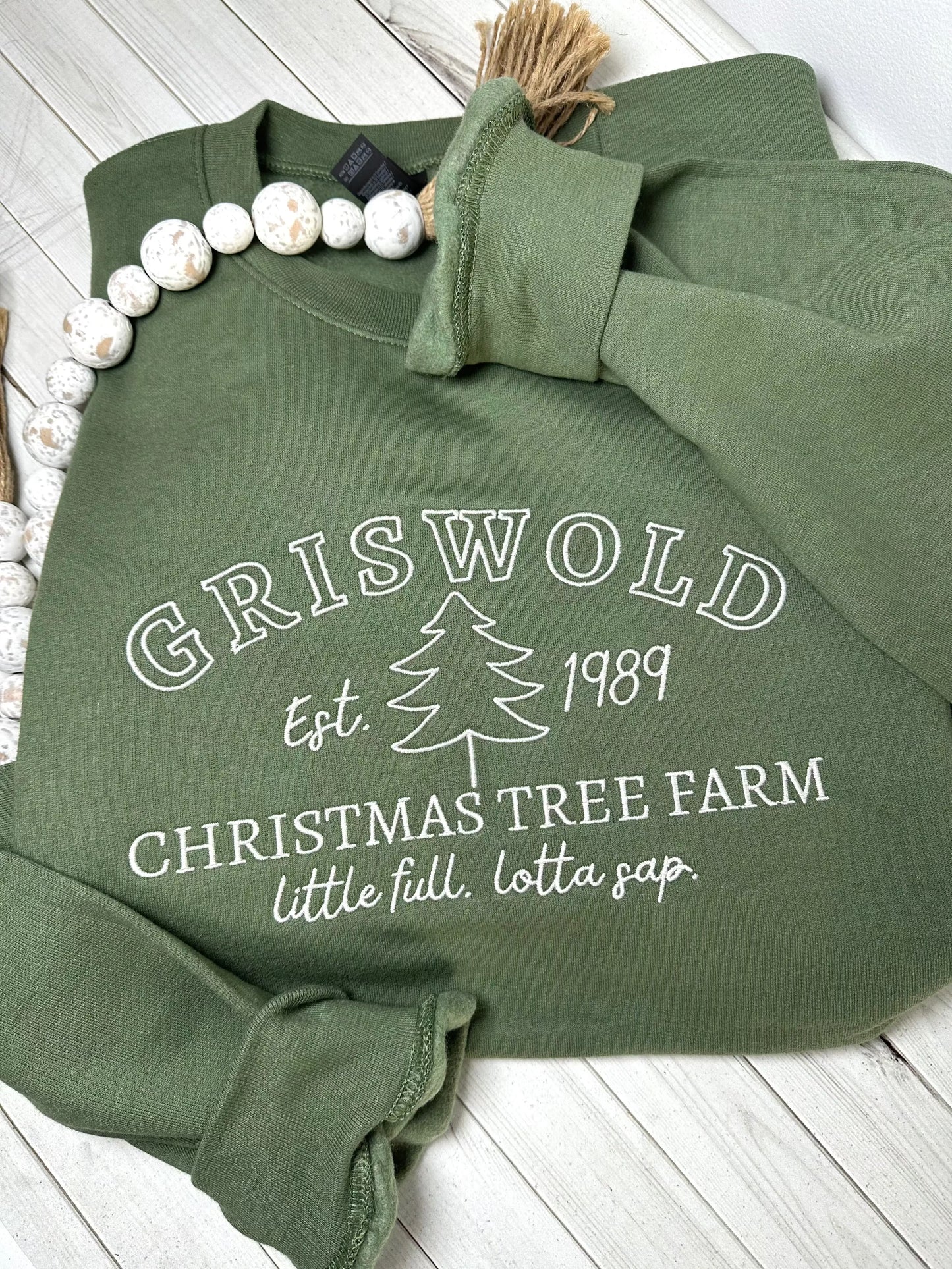 An army green sweatshirt with griswold Christmas tree farm embroidered on the front.