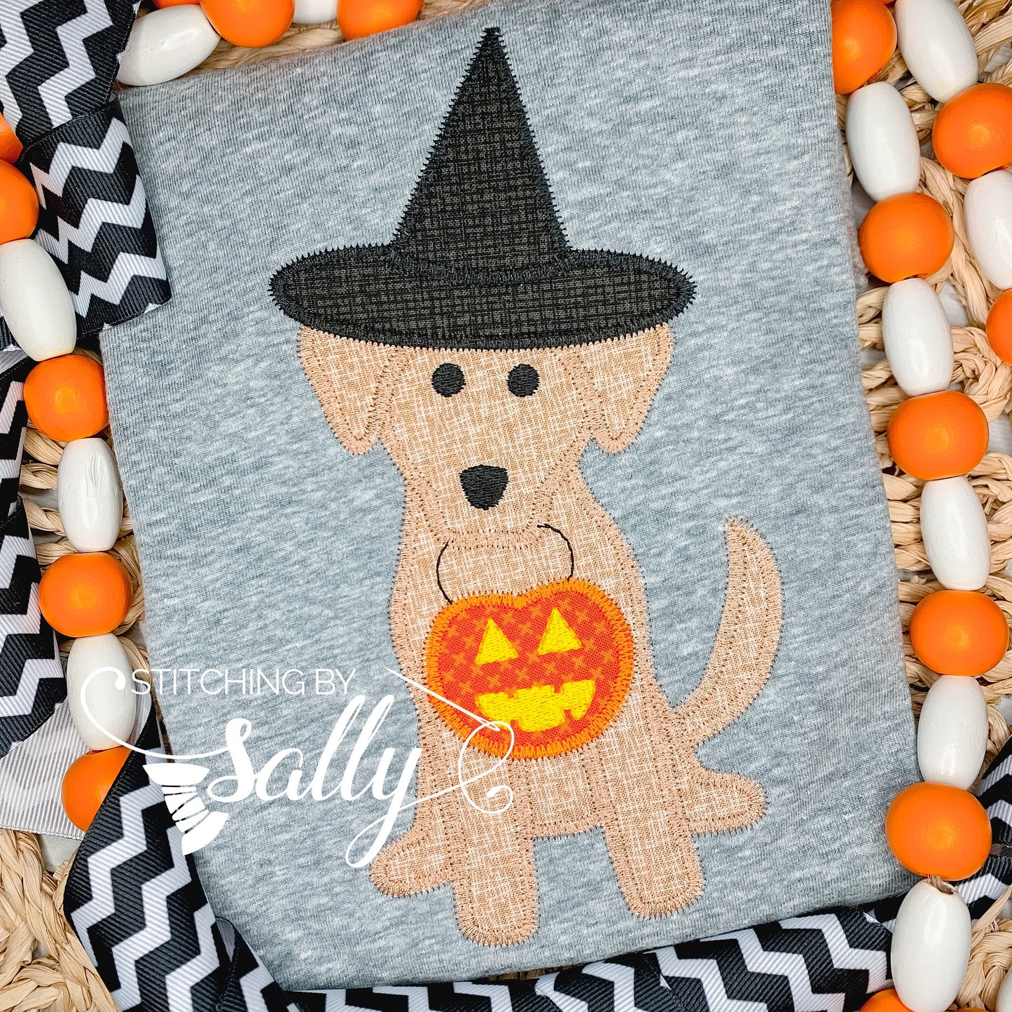 Brown dog holding a treat bag with a witch hat on. Appliquéd