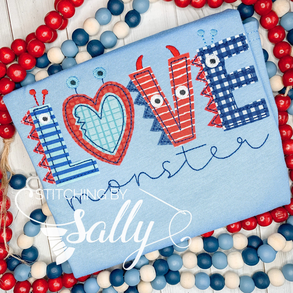 A blue shirt with love appliquéd in red and navy fabric. Monster is embroidered underneath.