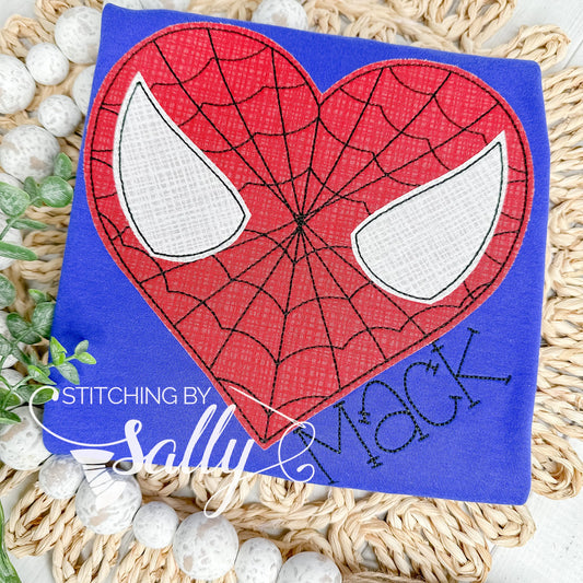 A blue shirt with a red heart appliqué that has a black embroidered web design.