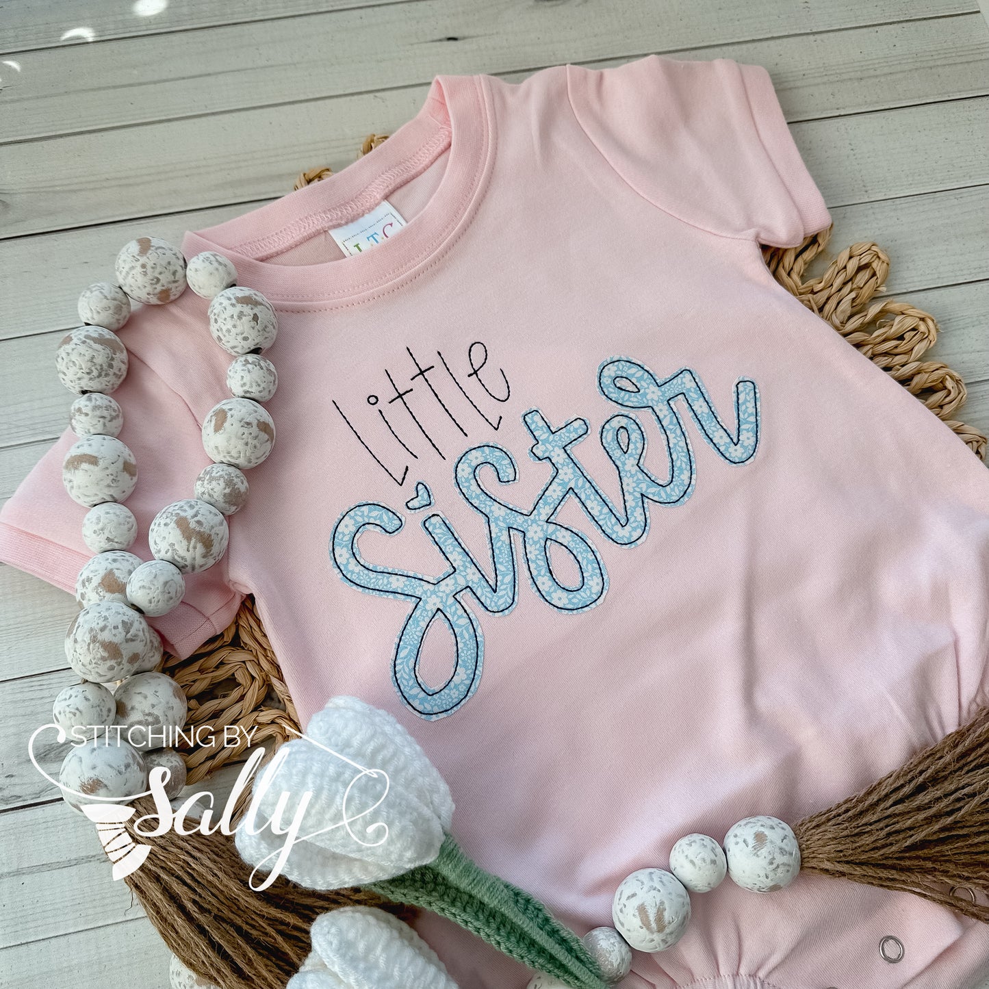 A pink romper with little sister appliquéd in pretty blue floral fabric