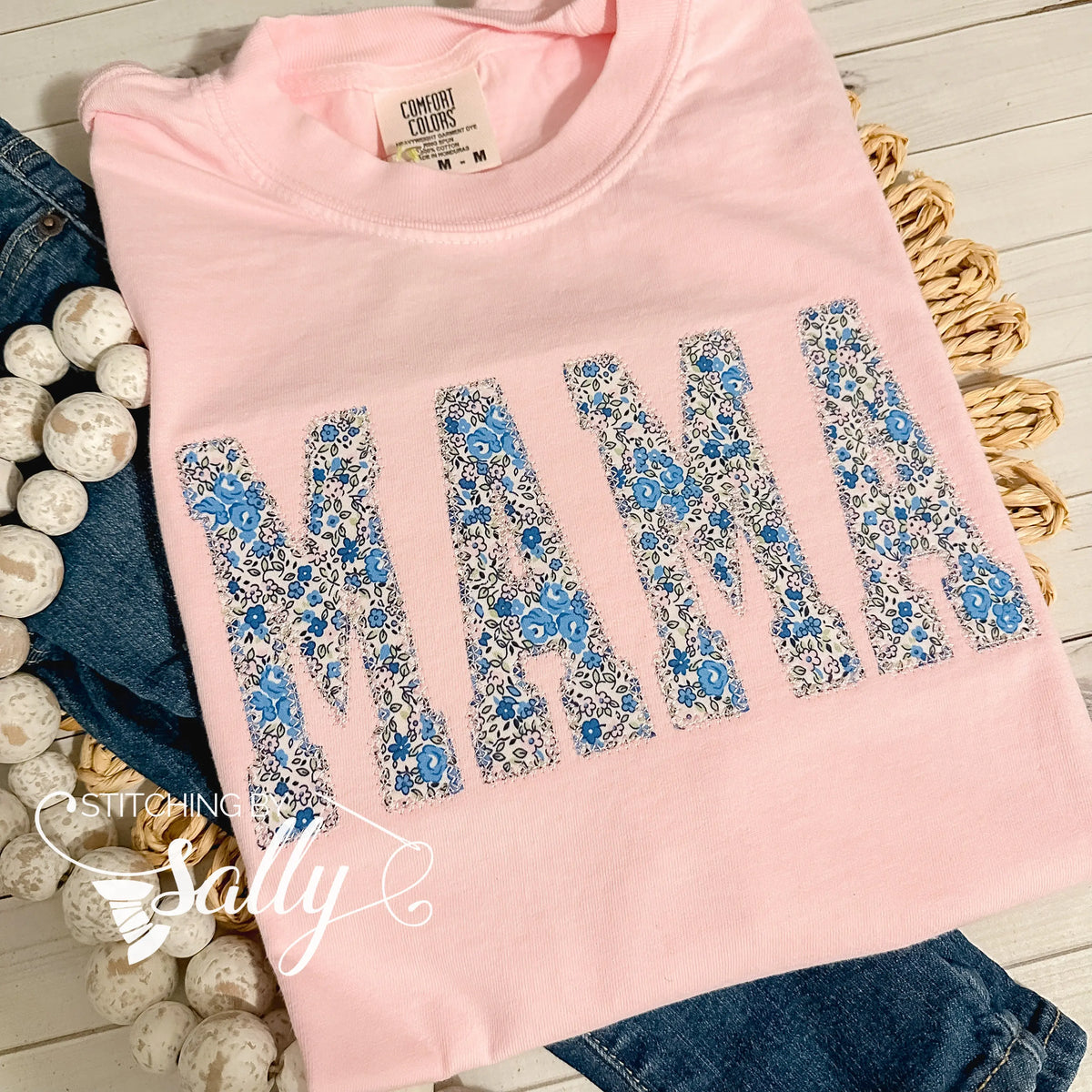 Light pink Comfort Colors shirt featuring 'Mama' appliqué in a beautiful blue and pink floral fabric, finished with a delicate diamond stitch in light pink thread for a soft, elegant touch. Perfect for mothers day.