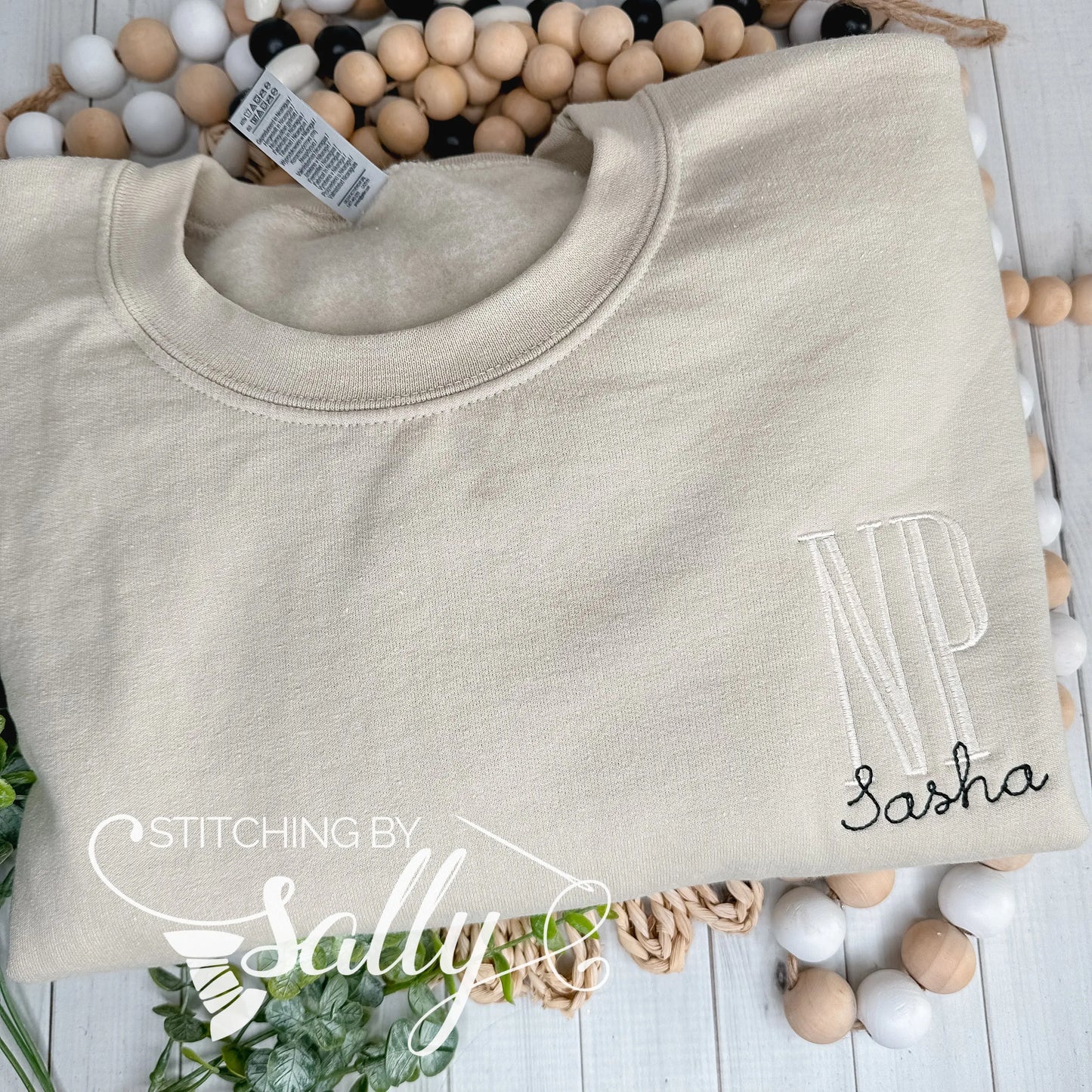 Flat lay of RN embroidered in ivory thread on a cream colored sweatshirt.