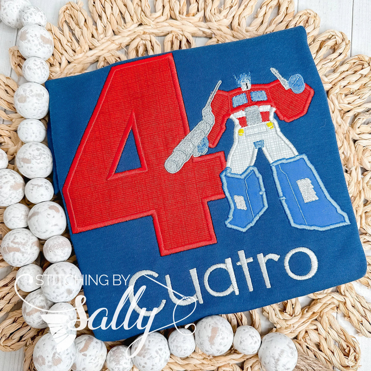 A navy shirt with a red number and a transformer appliquéd to the shirt. A name is embroidered underneath for a custom birthday shirt.