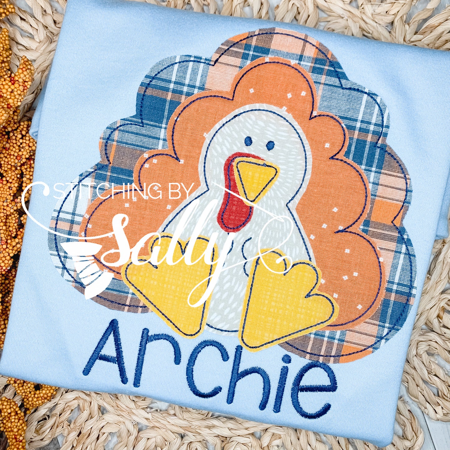 A boys' turkey applique shirt with a blue plaid background, featuring a yellow and white turkey design and the name 'Archie' sewn on the front.