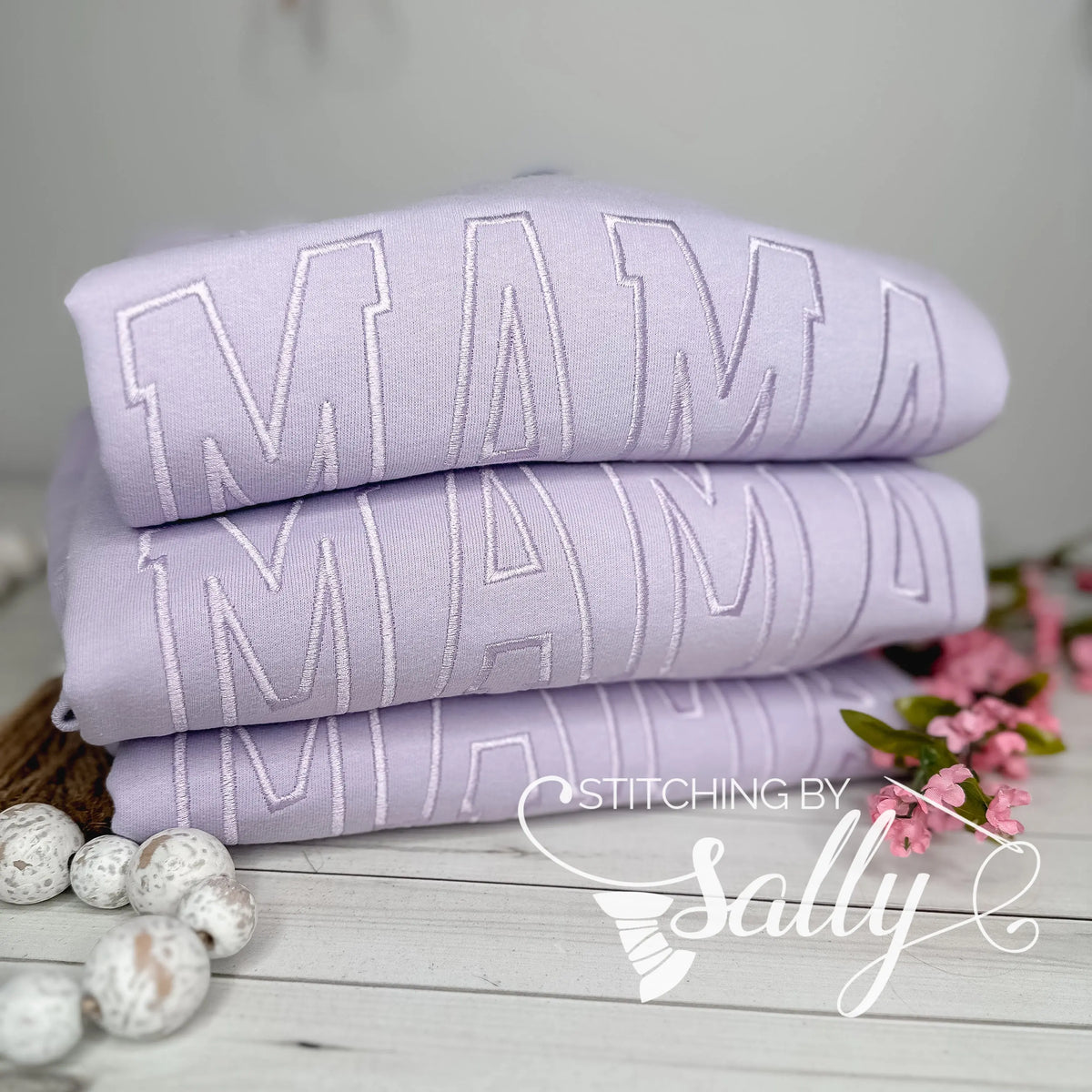 Close-up of lavender thread embroidered "MAMA" design, stack of three
