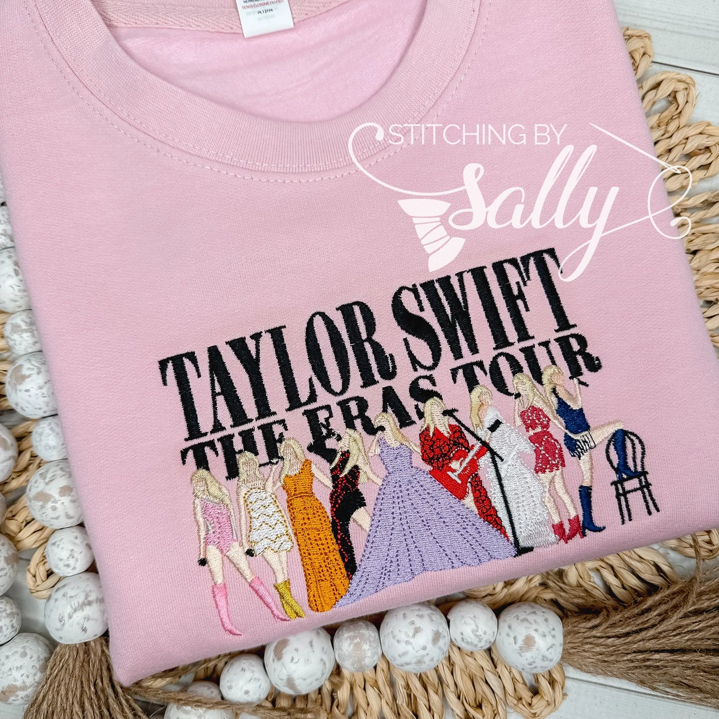 Taylor Swift the Eras Tour is embroidered along with different outfits for each era on a light pink youth sweatshirt.