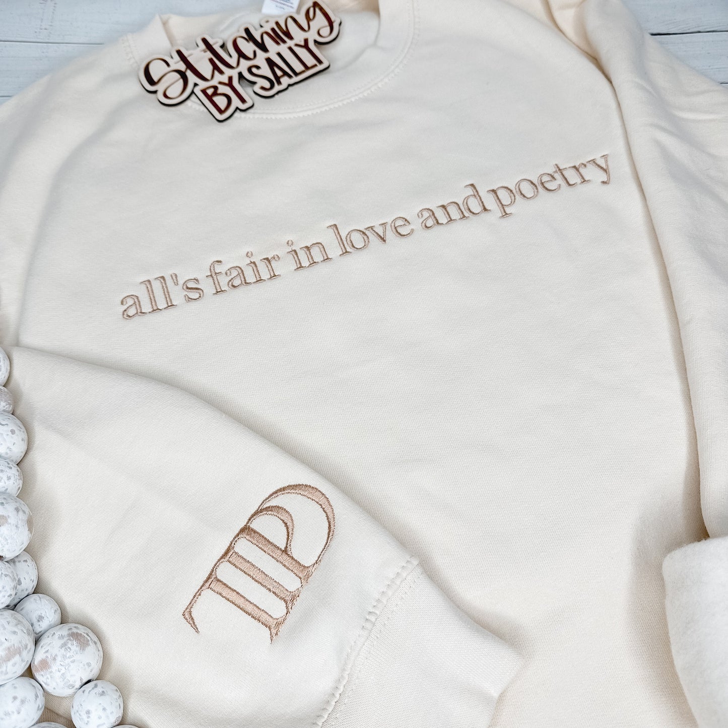 A cream sweatshirt with All is fair in love and poetry embroidered in tan thread for a minimalistic look