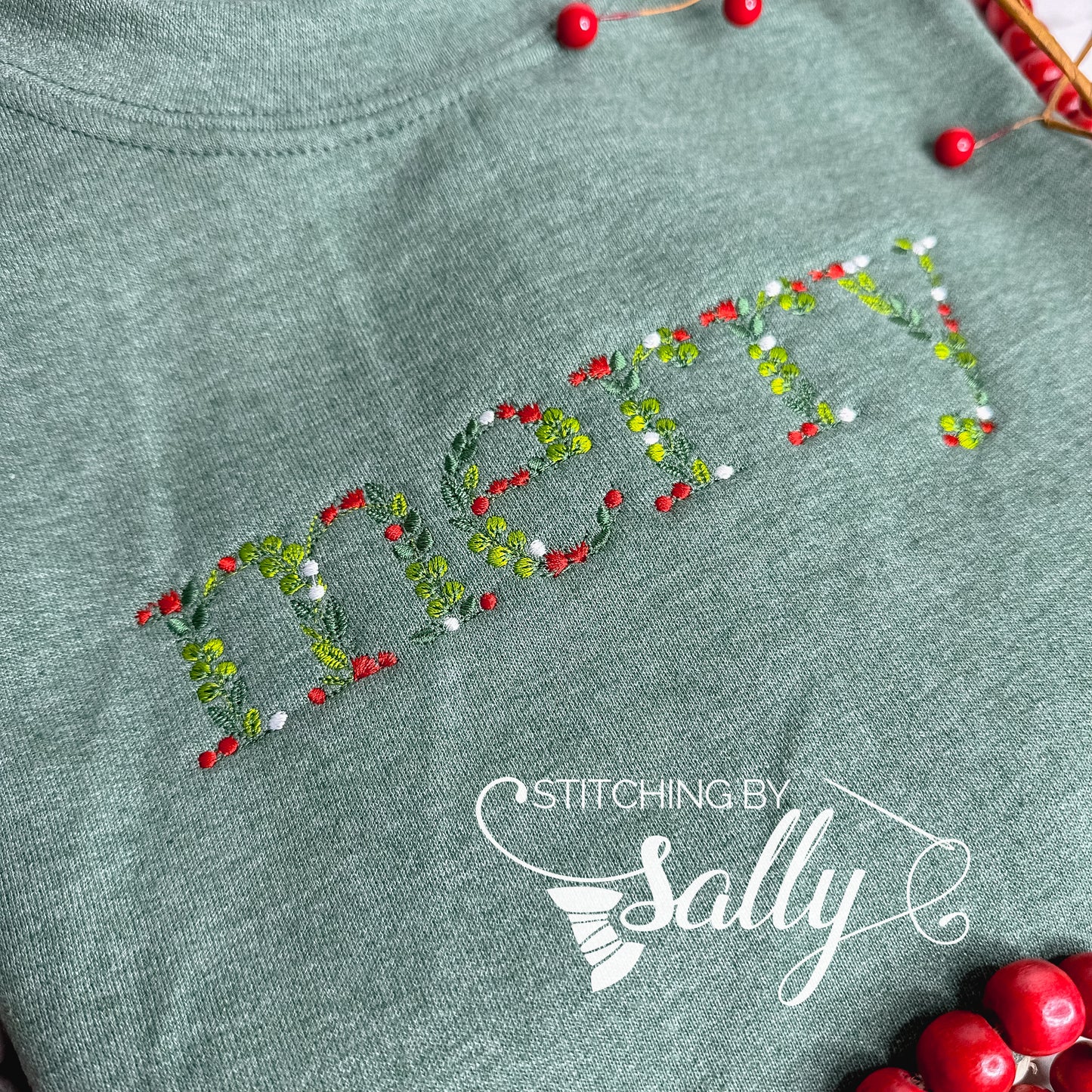 A green sweatshirt with "merry" embroidered in festive leaves and berries font, perfect for adding a touch of cheer to your wardrobe. Stitching by Sally