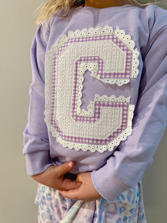 Large variety letter C applique with an eyelet lace detail around the letter on a purple sweatshirt. 