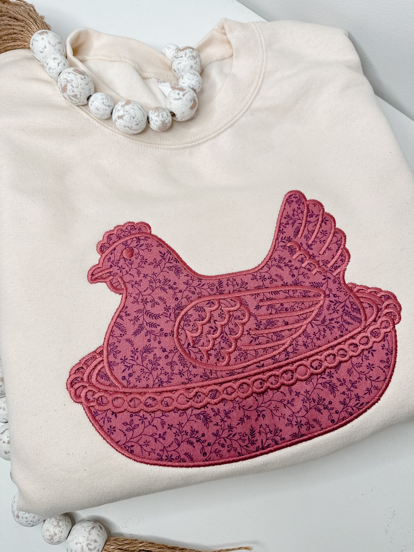 Beige sweatshirt with vintage "hen on a nest" appliqué design in maroon floral vine fabric. 