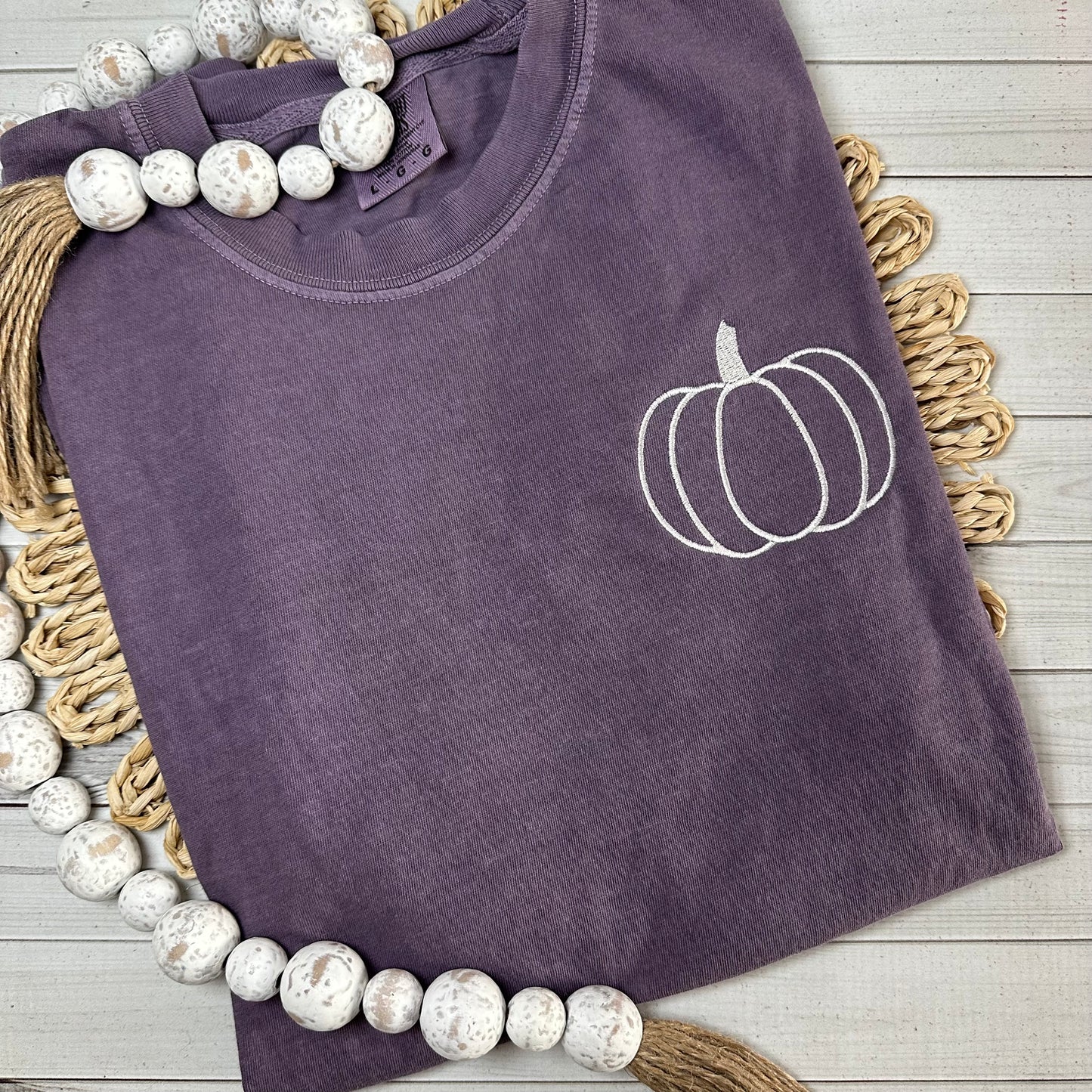 Berry colored tee shirt with a pumpkin embroidered in cream thread. 