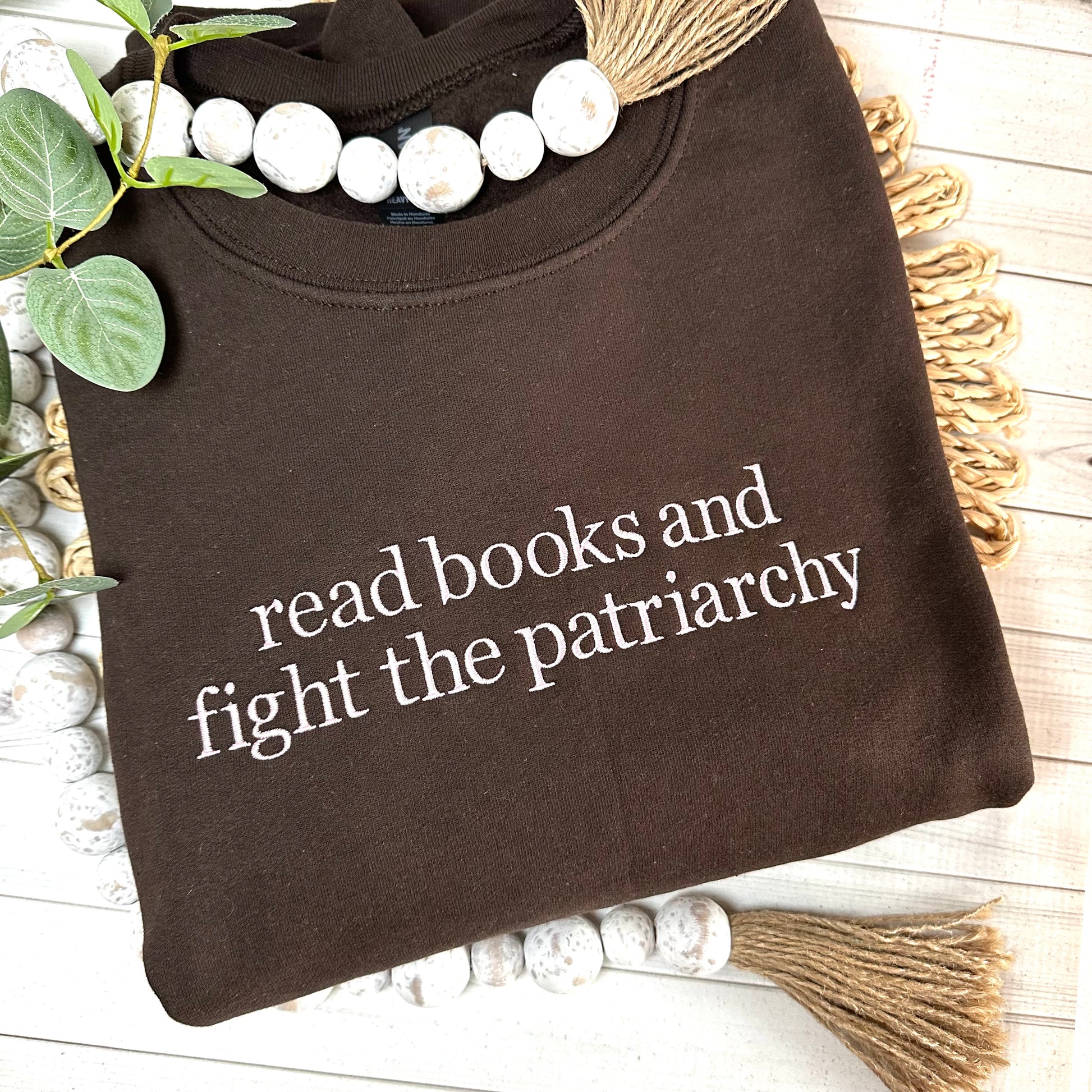 Brown sweatshirt with read books and fight the patriarchy embroidered in light pink thread. 