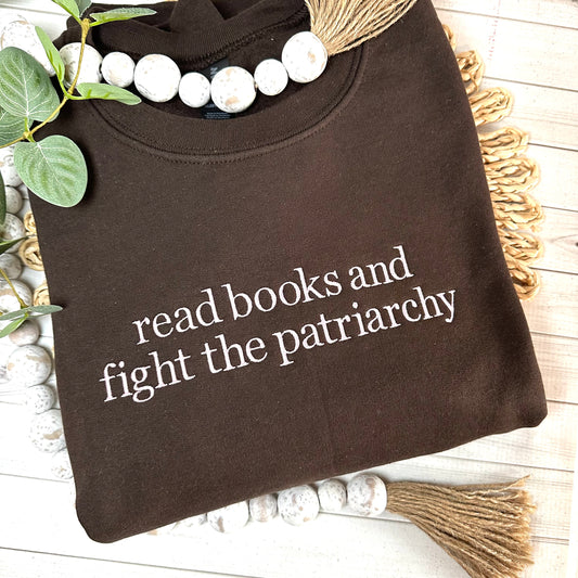 Brown sweatshirt with read books and fight the patriarchy embroidered in light pink thread. 