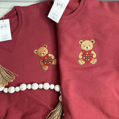 A bear with a box of chocolates embroidered onto a sweatshirt