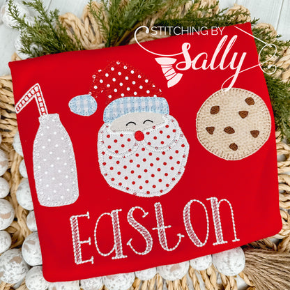 A red shirt with a milk jug, jolly santa, and a chocolate chip cookie appliquéd on. A name is embroidered underneath the design. 