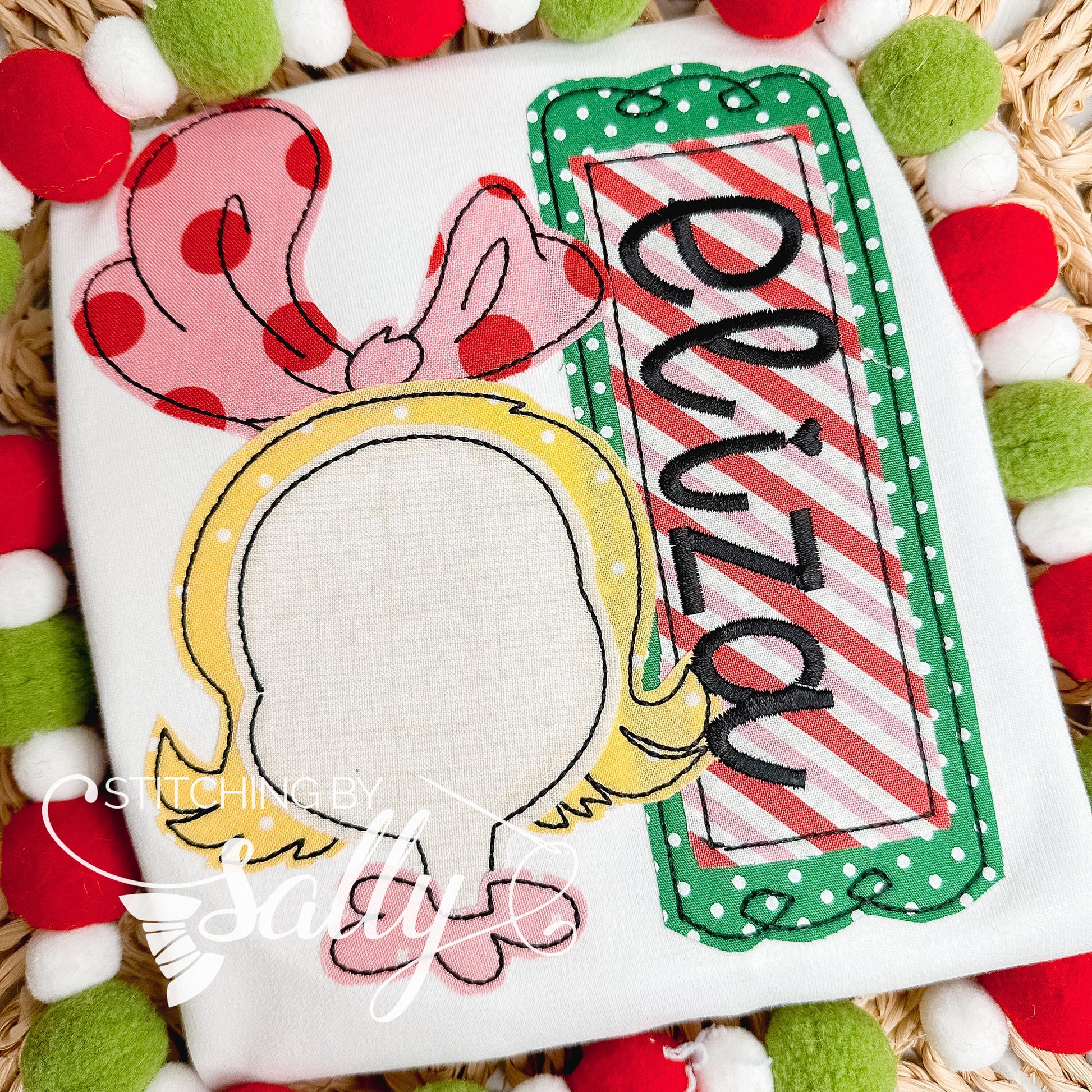 A white shirt with an inspired Cindy Lou drawing appliquéd with festive red, green and pink fabric. 