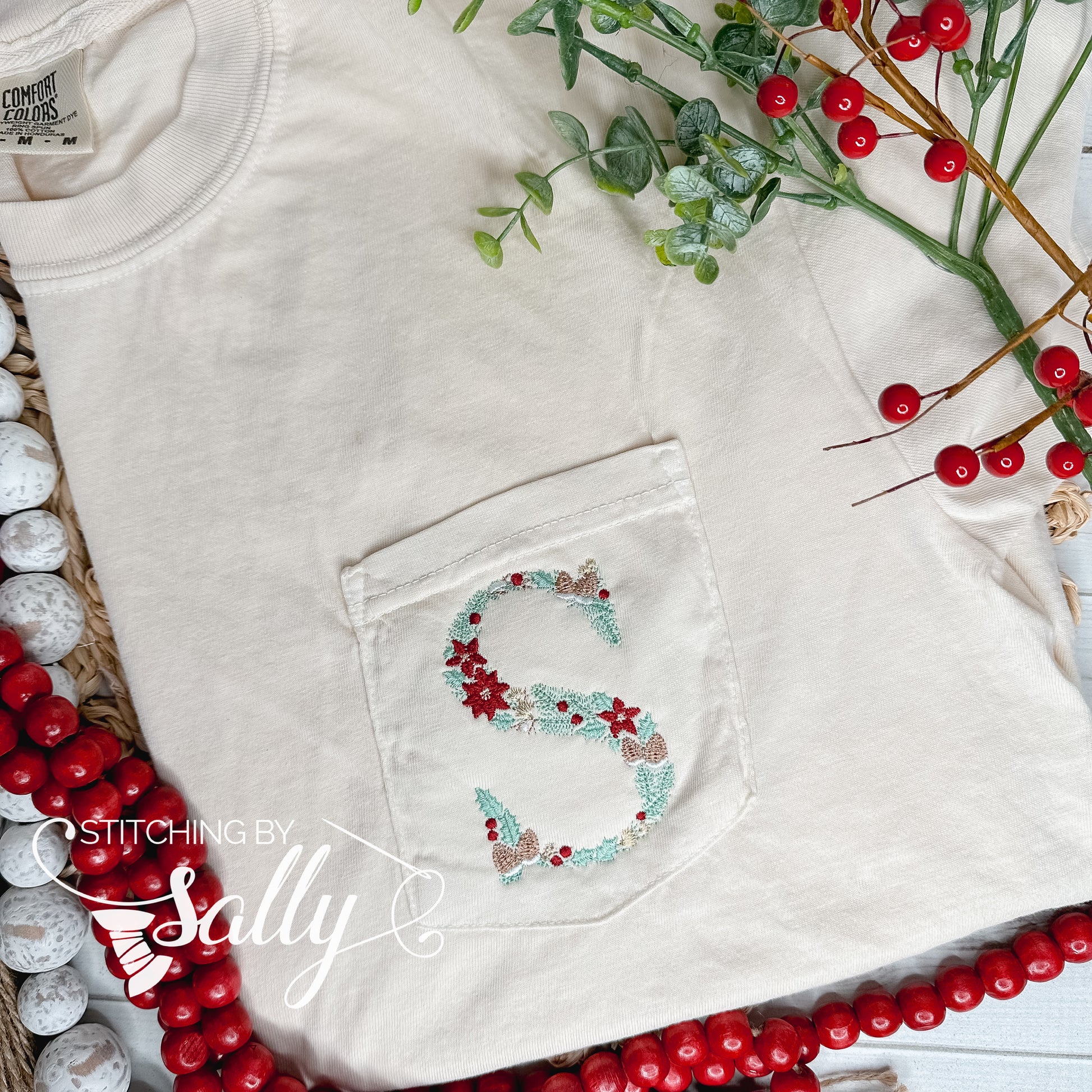 An ivory shirt with a custom “S” embroidered in Christmas floral letters on the pocket of the tee shirt. 