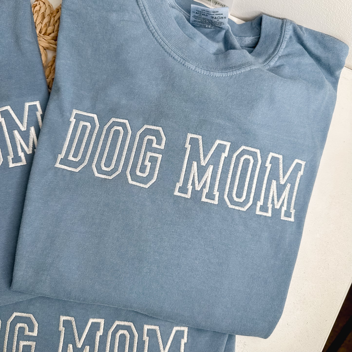 Folded blue shirt with 'DOG MOM' text embroidered in white thread.