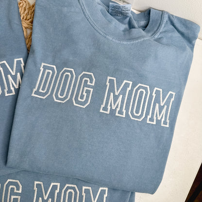 Folded blue shirt with 'DOG MOM' text embroidered in white thread.