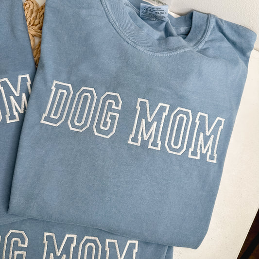 Folded blue shirt with 'DOG MOM' text embroidered in white thread.