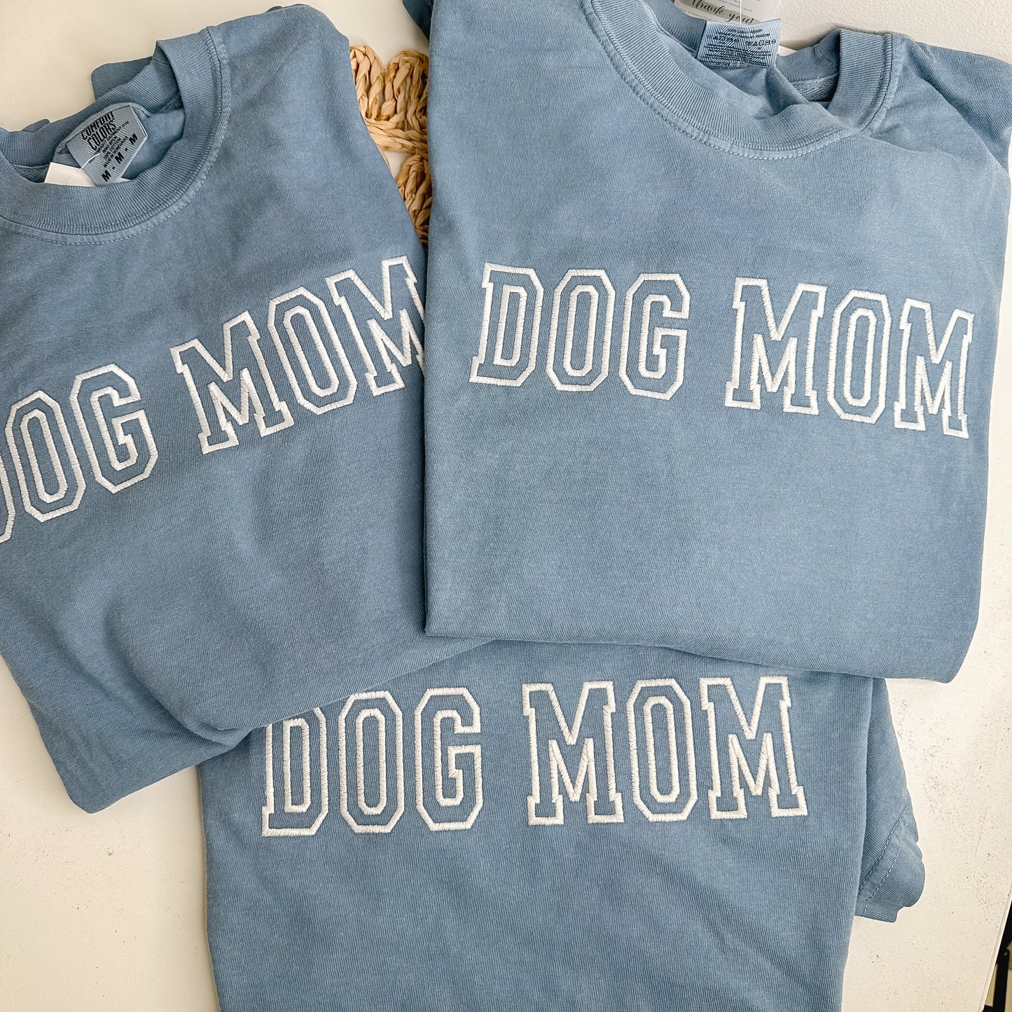 Three blue sweatshirts with 'DOG MOM' embroidered in white thread. 