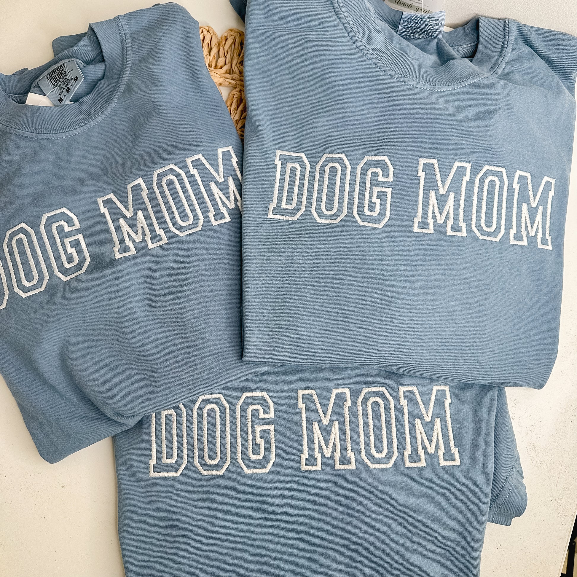 Three blue sweatshirts with 'DOG MOM' embroidered in white thread. 