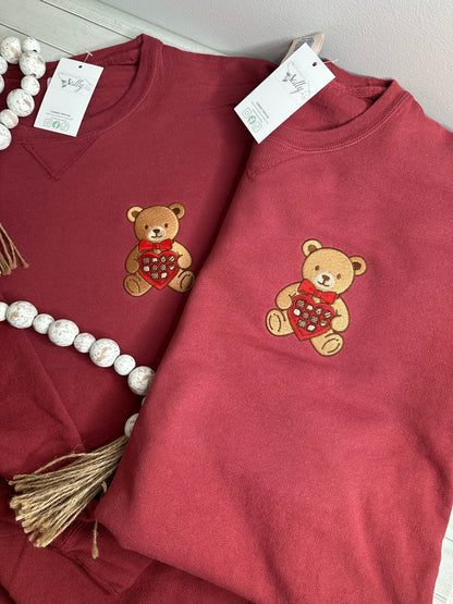 A bear with a box of chocolates embroidered onto a sweatshirt
