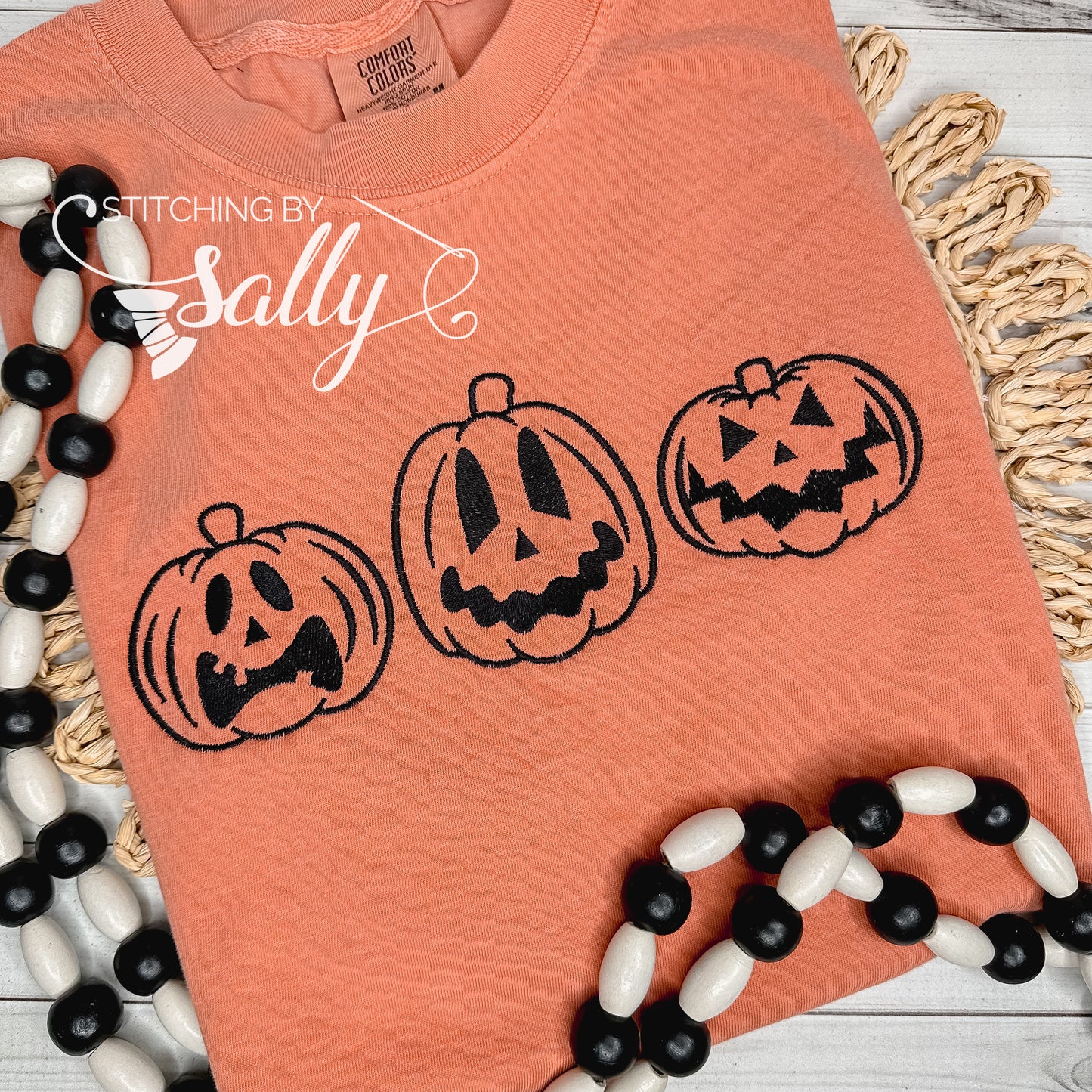 Jack o lanterns embroidered in black thread on an orange comfort colors shirt.