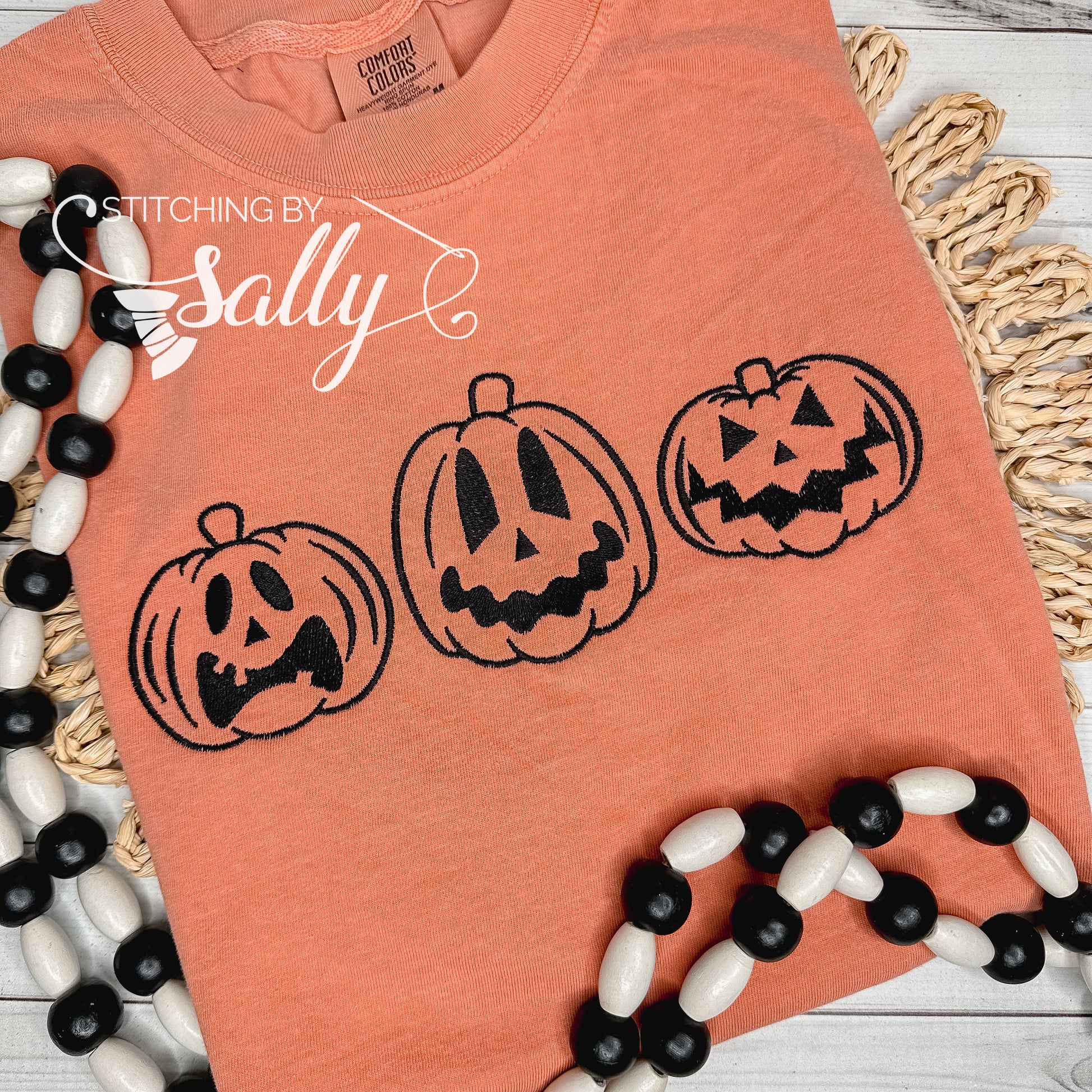 Jack o lanterns embroidered in black thread on an orange comfort colors shirt.