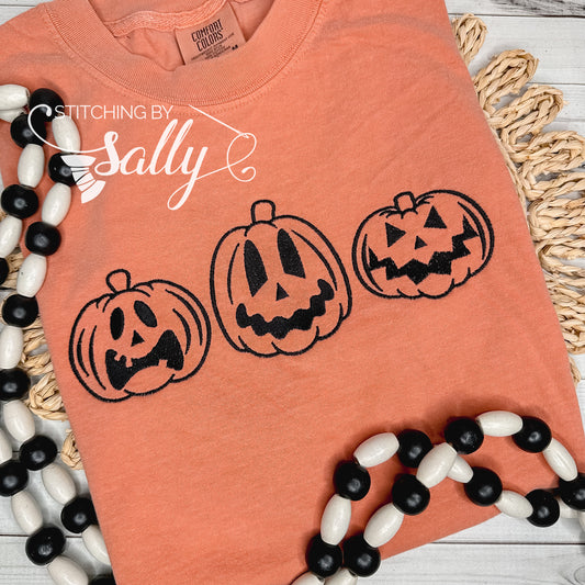Jack o lanterns embroidered in black thread on an orange comfort colors shirt.