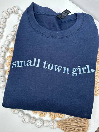 Folded navy blue sweatshirt with 'small town girl' embroidered.