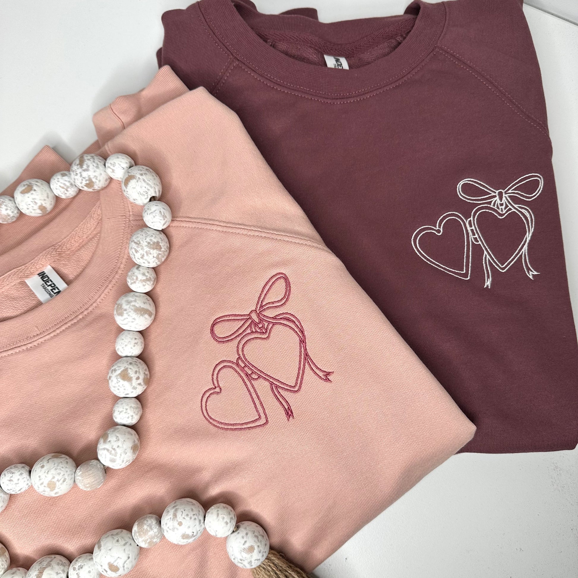 Heart locket embroidered on left chest of rose or maroon sweatshirt.