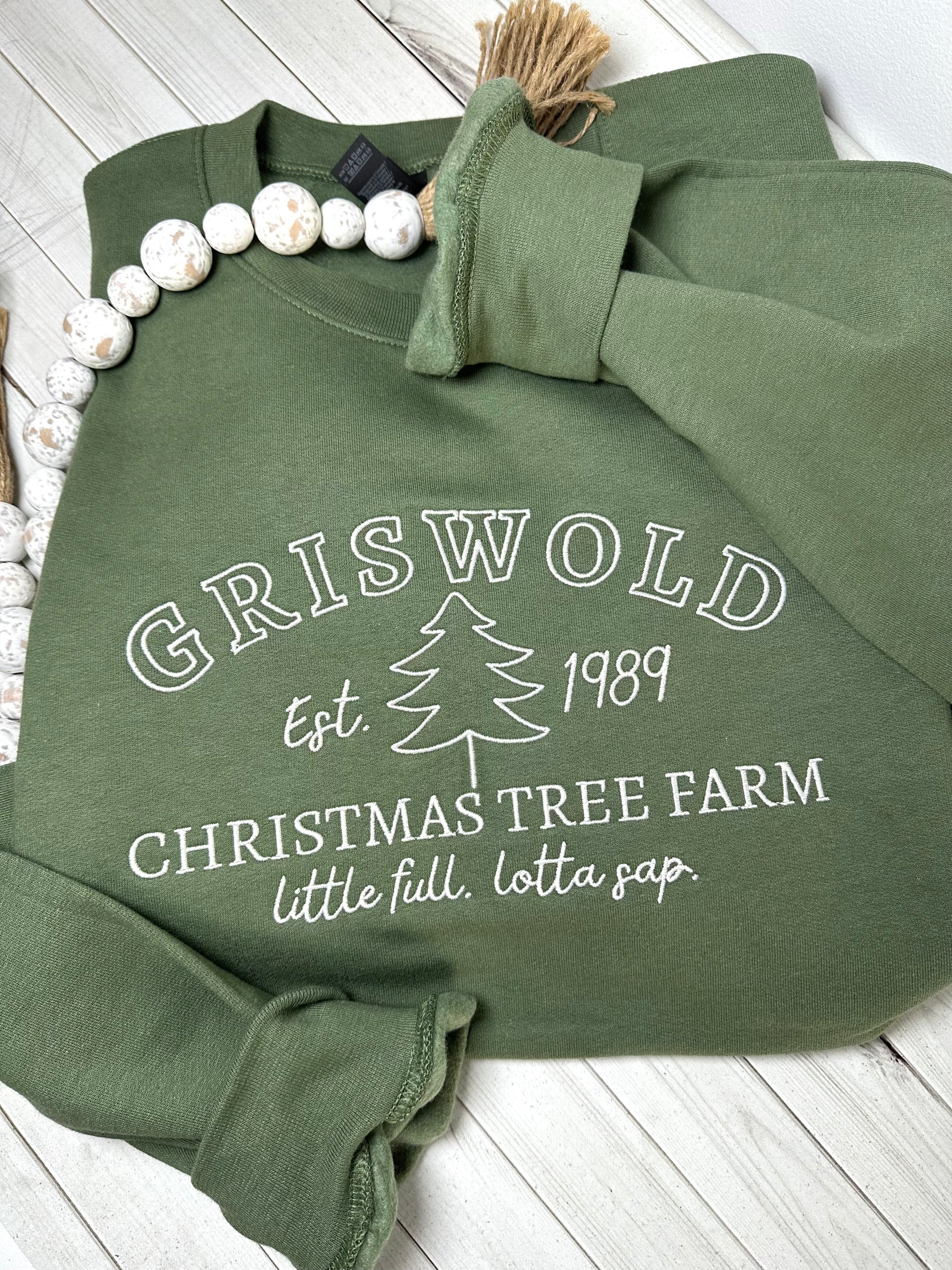 An army green sweatshirt with griswold Christmas tree farm embroidered on the front. 