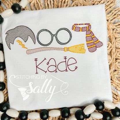 A white shirt with a few Harry Potter inspired designs embroidered on the shirt. A lighting bolt, glasses, scarf and a broom along with a name embroidered underneath. 
