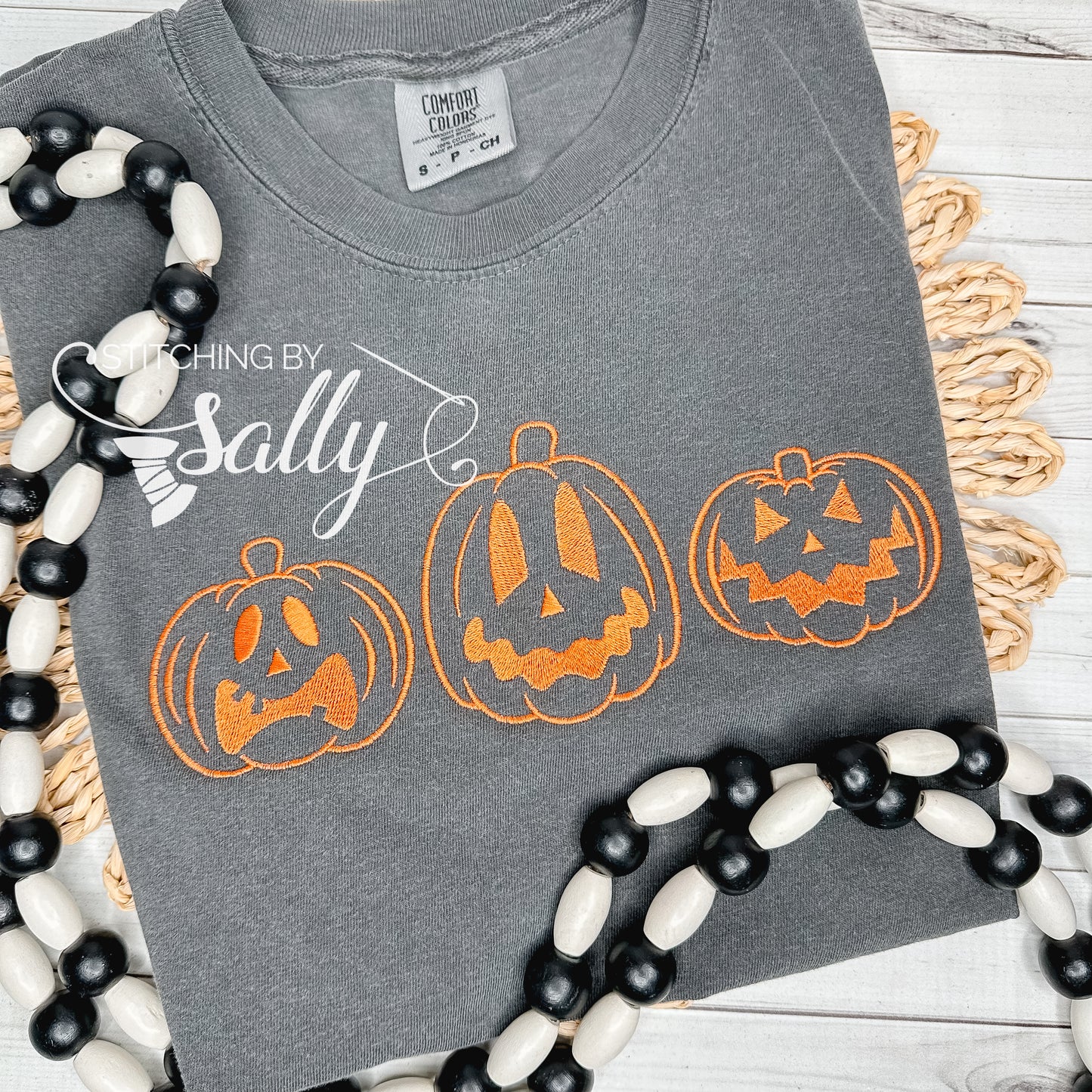 Embroidered jack o lanterns in orange thread on a dark grey comfort colors shirt.
