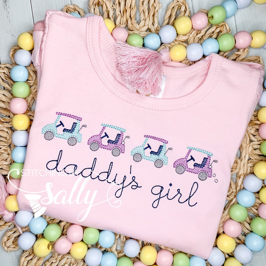 A girls pink shirt with four golf carts embroidered in a row in alternating teal and purple thread. Stitching by Sally 